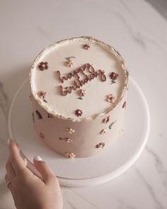 a hand is holding a cake with the word happy on it and flowers all over it