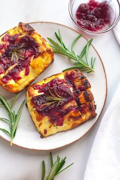 two pieces of bread on a plate with cranberry sauce and rosemary sprigs