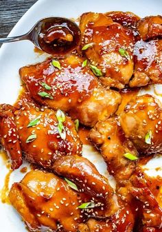 a white plate topped with chicken wings covered in bbq sauce and garnished with sesame seeds