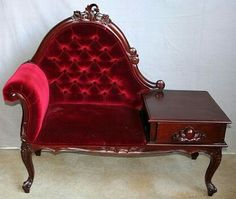 a red velvet couch sitting on top of a wooden table next to a white wall