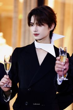 a woman in a suit holding two wine glasses and looking at the camera with one hand on her hips