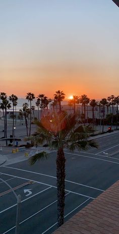 the sun is setting over an empty parking lot with palm trees in the foreground