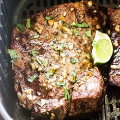 two steaks cooking on the grill with garnishes and lemon wedges