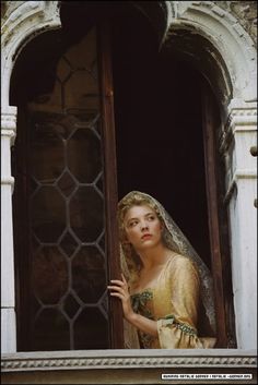 a woman in a wedding dress looking out an open window with her veil draped over her head