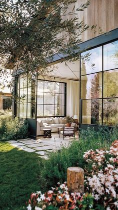 an outside view of a house with lots of windows and flowers in the front yard