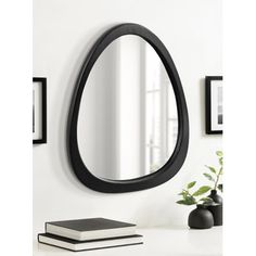 a black oval mirror sitting on top of a white table next to a book and vase