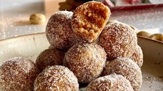 a pile of powdered sugar donuts sitting on top of a white plate next to nuts