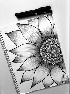 a black and white drawing of a sunflower on top of a notebook next to a pen