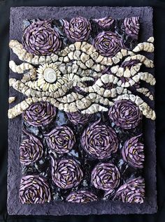 an art work made out of purple flowers and shells on a black cloth with white buttons