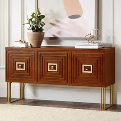 a plant is sitting on top of a wooden sideboard in front of a painting