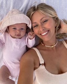 a woman laying on top of a bed next to a baby wearing a pink hat