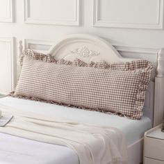 a bed with a white headboard and brown checkered pillow on top of it