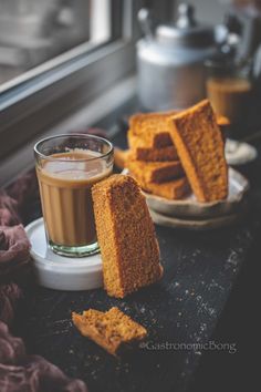 a cup of coffee and some pieces of bread on a table next to a window