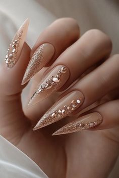 Add drama to your look with these nude stiletto nails, enhanced with glittering rose gold designs. Perfect for elegant winter nails or a trendy goth winter vibe. Find more trendy winter nails at nailhow.com. Save this gorgeous pin for later! 🌟❄️. Champagne Stilleto Nails, Nail Ideas For Champagne Dress, January Stiletto Nails, Elegant Nails Classy 2024 Almond, Nude And Gold Almond Nails, Classy Elegant Nails Vintage, Trendy Winter Nails 2025, New Years Coffin Nails, Baddie New Years Nails