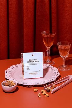 a table topped with wine glasses and plates filled with nuts next to a menu on a plate