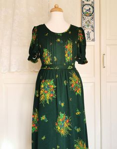 Beautiful green floral dress. The dress has a lining and a zipper at the back. I think the fabric is one cotton and wool blend, but I'm not sure. The fabric is supple and has minimal stretch. The zipper seems to pull a bit on the fabric (see photo), but the dress is also a bit loose on the mannequin. Sizes only measured: Armpit 43 cm Waist 35 cm Length 130 cm Falls approximately like S/M Has a ribbon at the waist and can therefore be tied to size Green Floral Print Dress For Daywear, Green Lined Dress For Garden Party, Green Lined Dresses For Garden Party, Green Cotton Floral Dress For Garden Party, Vintage Green Floral Print Dress, Green Cotton Floral Short Sleeve Dress, Green Cotton Floral Dress With Short Sleeves, Green Floral Print Cotton Dress, Green Cotton Floral Print Dress