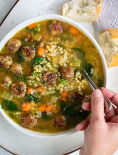 a person holding a spoon in a bowl of soup with meatballs and veggies