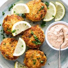 crab cakes with tartar sauce and lemon wedges on a plate next to a spoon