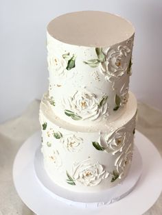 a three tiered cake with white flowers on it sitting on a plate in front of a wall