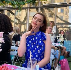 a woman sitting at a table with food in front of her and other people standing around