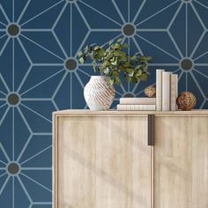 a wooden cabinet with books and a vase on it next to a blue geometric wallpaper