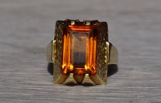 The Whitsett: Ladies Mid Century Citrine Cocktail Ring in 14K Yellow Gold. Crafted in 14 karat white gold is this mid century style statement ring. Set in the center of this ring is a 13mm x 9mm emerald cut citrine. The ring is stamped Germany and is currently a finger size 7.5 yet can be adjusted in size for an additional charge upon request. Love this piece, but don't have the money to spend right now?  We offer FREE layaway on every item in our shop.  With just 20% down, take one full year (i Retro Polished Rings For Formal Events, Retro Formal Rings With Polished Finish, Retro Rings With Polished Finish For Formal Occasions, Modern Formal Hallmarked Topaz Ring, Retro 14k Gold Formal Rings, Retro 14k Gold Rings For Formal Occasions, Modern Citrine Rings For Formal Occasions, Formal Retro 14k Gold Rings, Retro Orange Jewelry For Formal Events