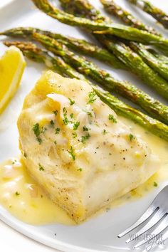 a white plate topped with fish and asparagus next to a lemon wedged slice