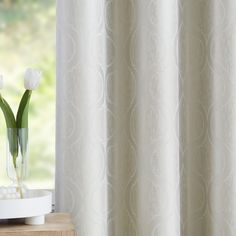 two white tulips are in a vase on a table next to a window