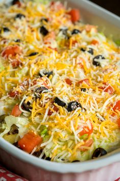 a casserole dish with cheese, olives, tomatoes and other toppings