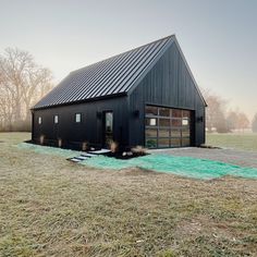 a black barn sits in the middle of a field