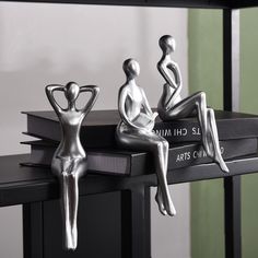 three silver figurines sitting on top of books