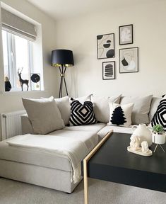 a living room with white couches and black table in front of the window, framed pictures on the wall