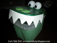 a green and white plastic container with eyes and teeth on it's lid, sitting on a black surface