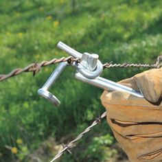 a close up of a metal barbwire fence with a bag on it and grass in the background