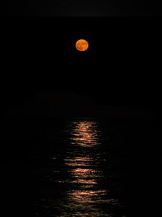 the full moon is seen over the ocean at night with its reflection in the water