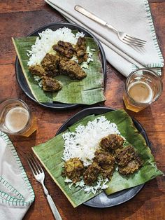 two plates filled with meat and rice on top of a wooden table next to silverware