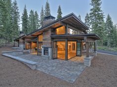 a large house sitting on top of a dirt field next to pine trees and a forest