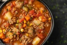 a bowl filled with meat and vegetable soup on top of a table next to a spoon