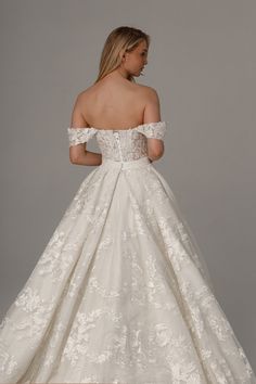 a woman in a white wedding dress with off the shoulder sleeves and flowers on it