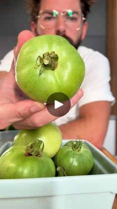 a man is holding up some green tomatoes