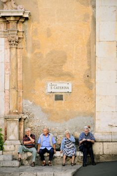 four elderly people sitting on steps in front of an old building with a sign that reads la catena