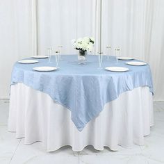 a blue and white table cloth on top of a round table with place settings in front of it