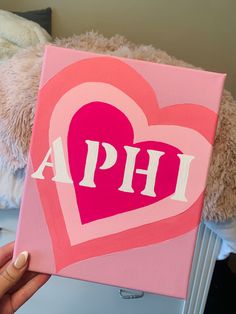 a person holding up a pink heart with the word aph painted on it in front of a teddy bear