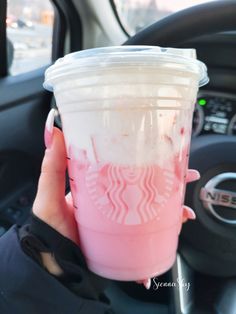 a woman holding up a pink starbucks drink in her hand while sitting in the driver's seat of a car