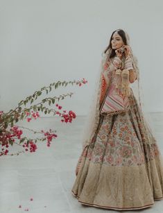 a woman standing in front of flowers wearing a wedding dress and holding a cell phone to her ear