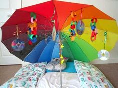 an upside down rainbow colored umbrella sitting on top of a bed with pillows and blankets