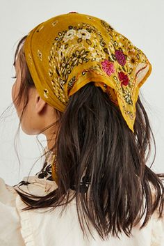 a woman with long hair wearing a yellow head scarf on top of her head and looking off to the side