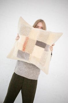 a woman holding up a pillow that is made out of squares and rectangles