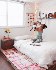 a person jumping on top of a bed in a room with white walls and string lights