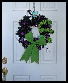 a green and black wreath hanging on the front door with purple and white decorations around it